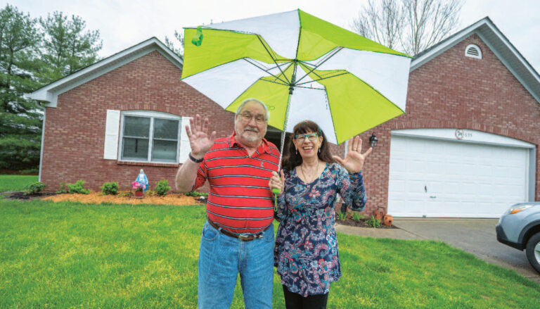 Two residents standing outside their Otterbein home holding an umbrella