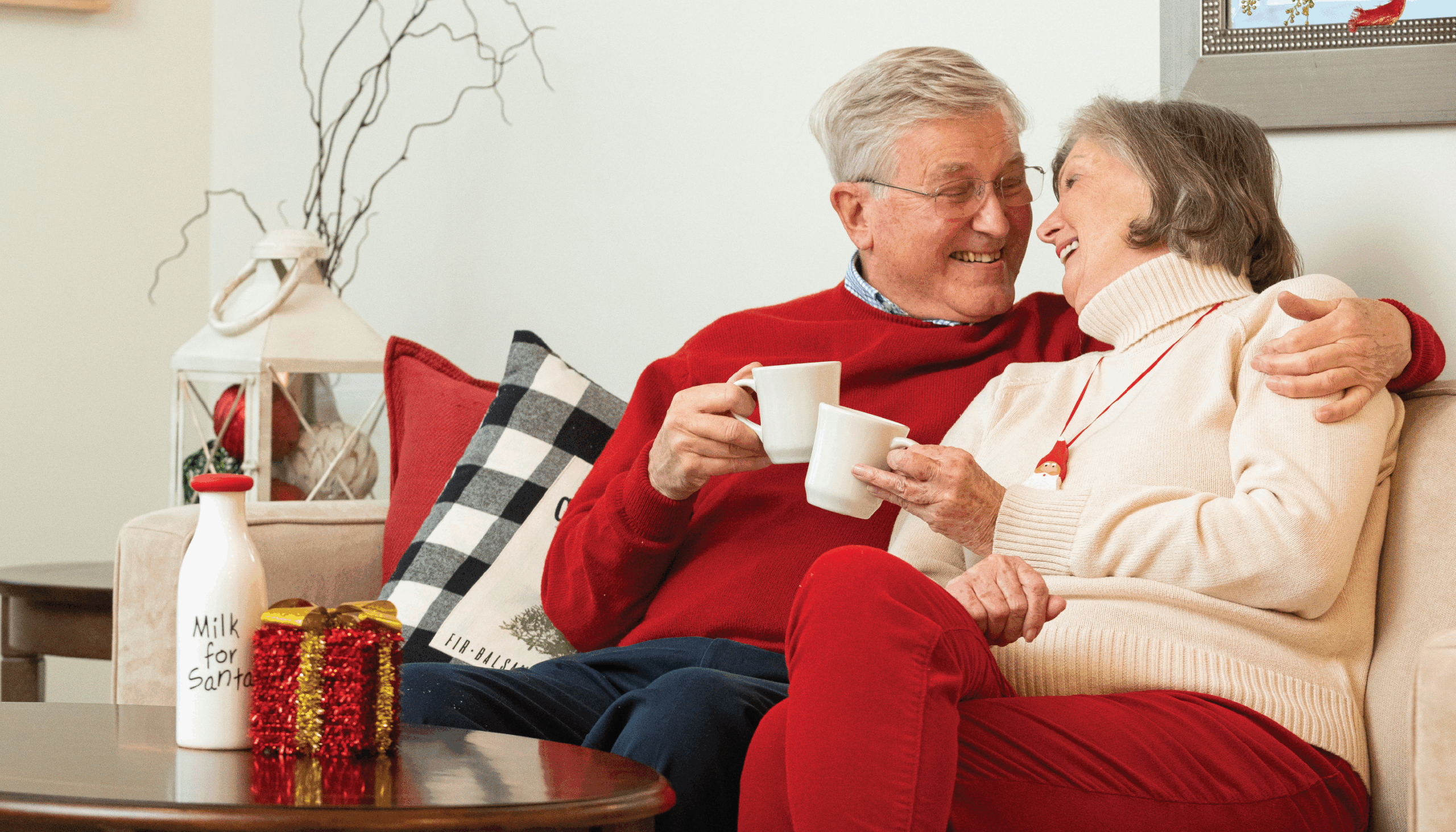A man and woman sitting on a couch clinking mugs