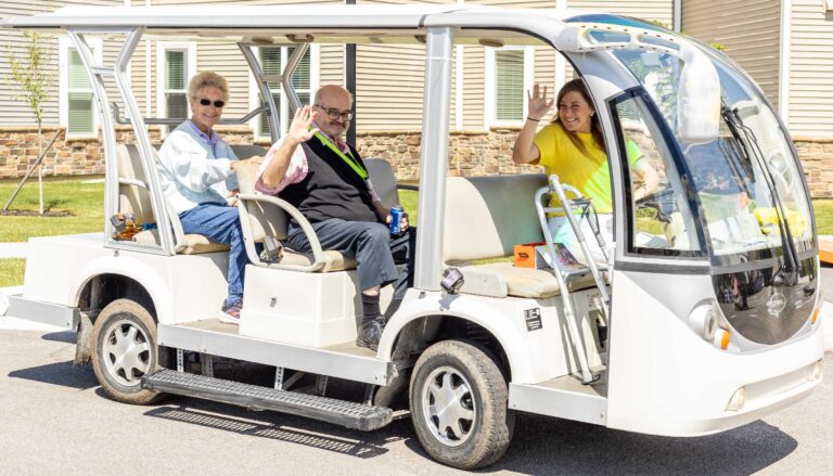 two Otterbein residents and a staff member driving a transportation cart