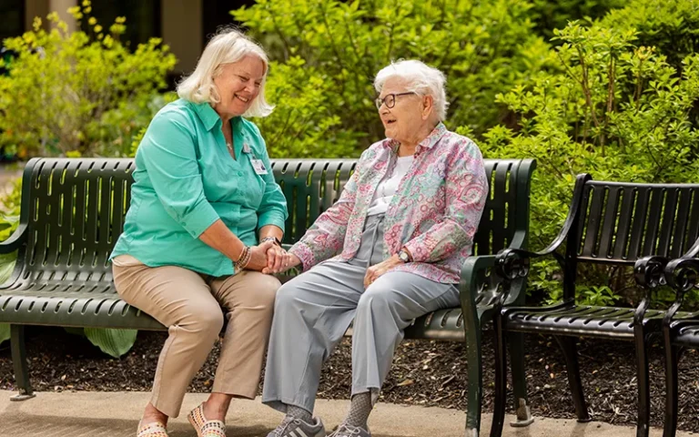 Otterbein partner holds hands with a resident while seated on a bench outdoors