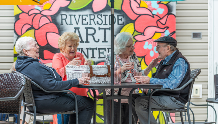 Carl and a group of friends having a picnic at an outdoor cafe and laughing. 