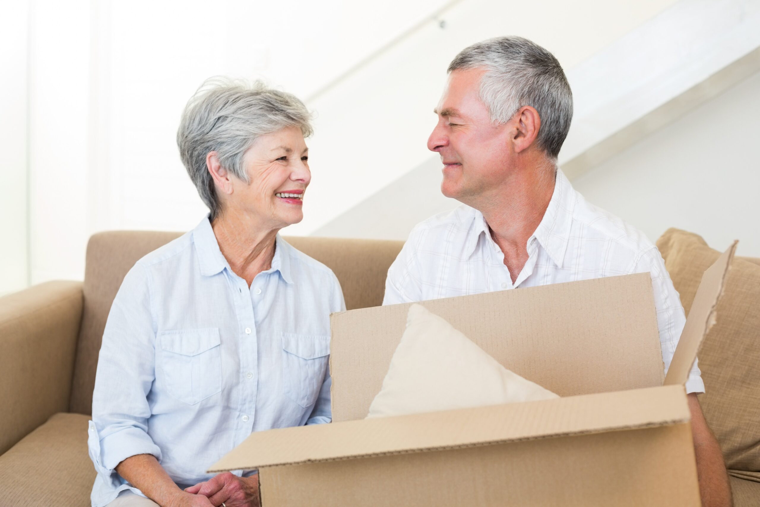 A man and woman sitting on a couch holding a box