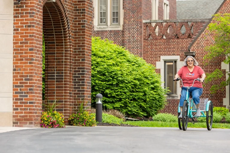 Otterbein resident riding a bicycle through a scenic pathway on Otterbein Sunset House grounds