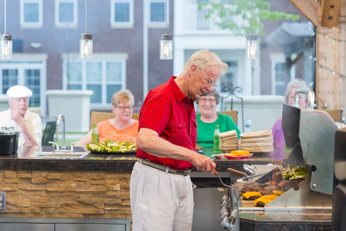 Otterbein Lebanon residents dine outdoors on the patio with one resident cooking on the grill