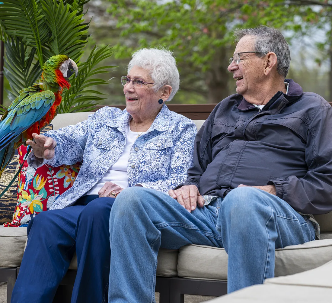 Otterbein Lebanon residents sit outdoors on a couch holding a bright bird