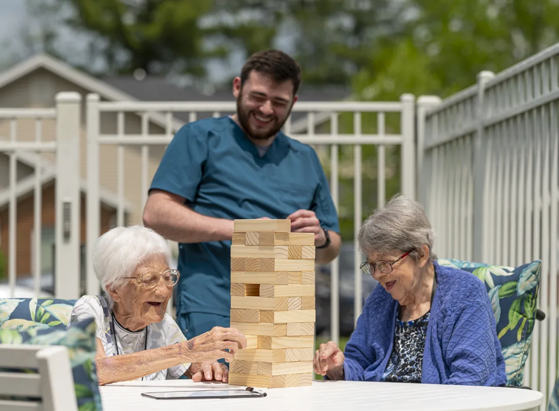 Otterbein small house elders play Jenga together on the outdoor patio as an elder assistant looks on