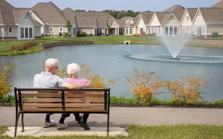 Otterbein resident couple sitting on bench together overlooking villas and the pond with a fountain