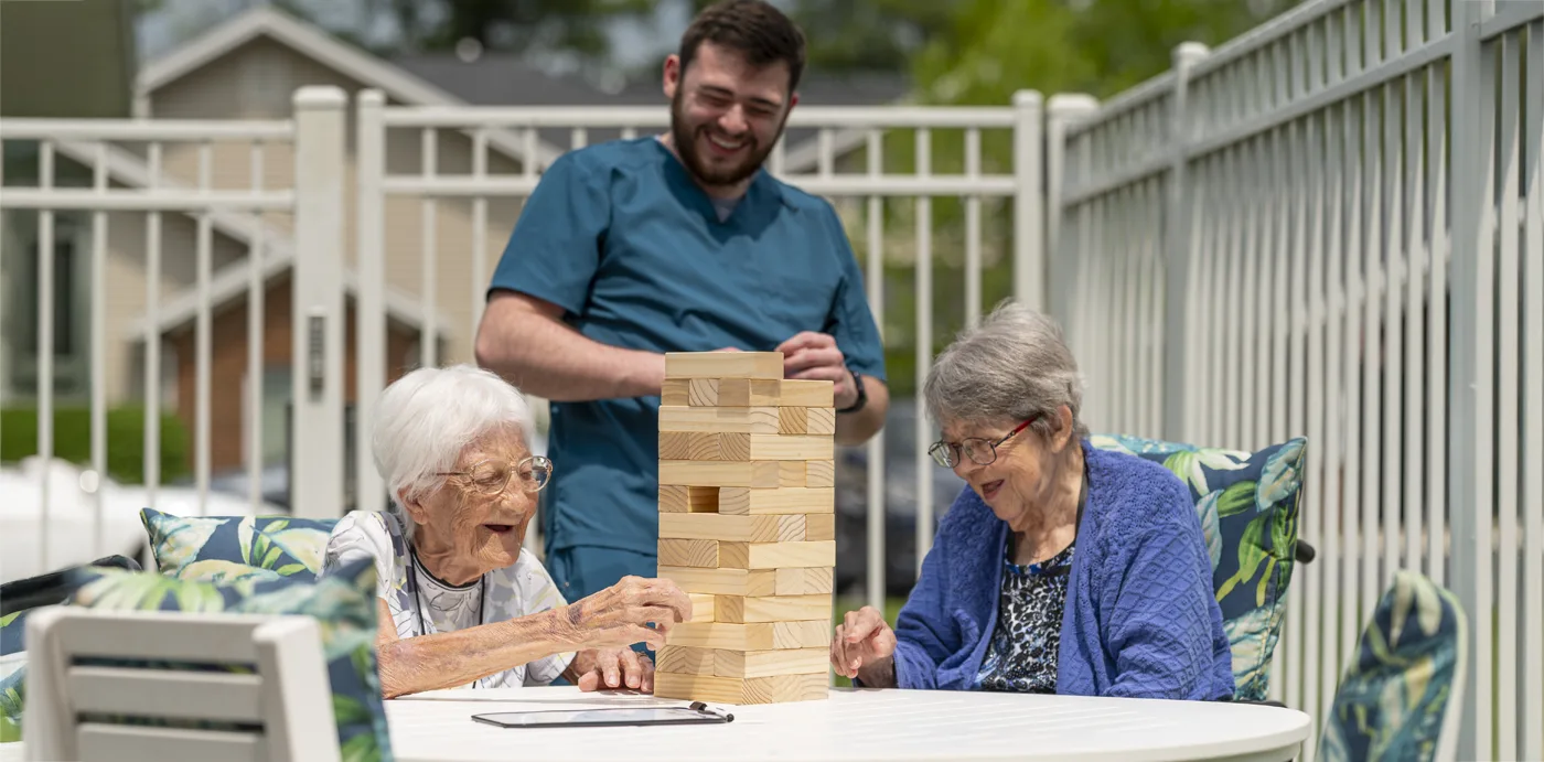 Otterbein small house elders play Jenga outdoors on the patio as elder assistant looks on