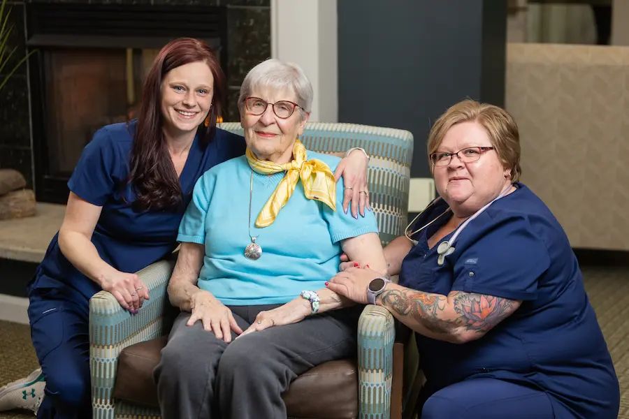 Otterbein North Olmsted resident sits on a chair with partners on either side of her embracing her