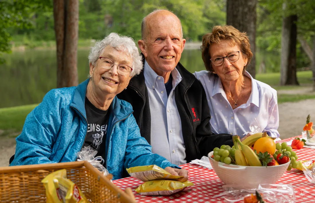Otterbein Sunset Village residents seated together for a picnic near a wooded area with a water view