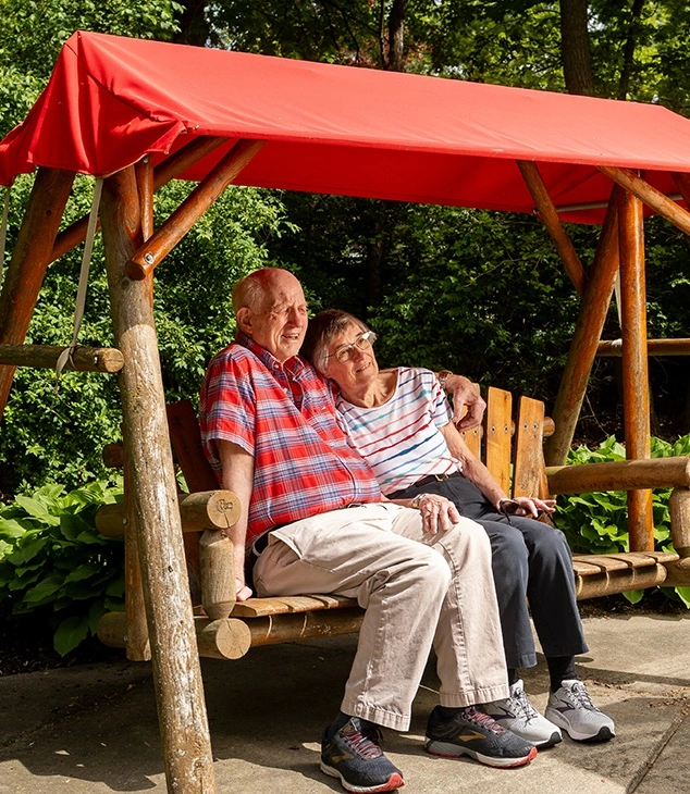 Otterbein Sunset House resident couple sitting on a wooden swing in a wooded area
