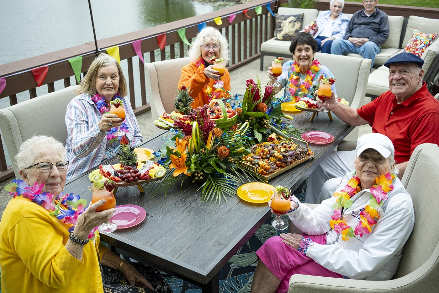 Small group of residents enjoy drinks wearing colorful leis outside on the waterfront patio