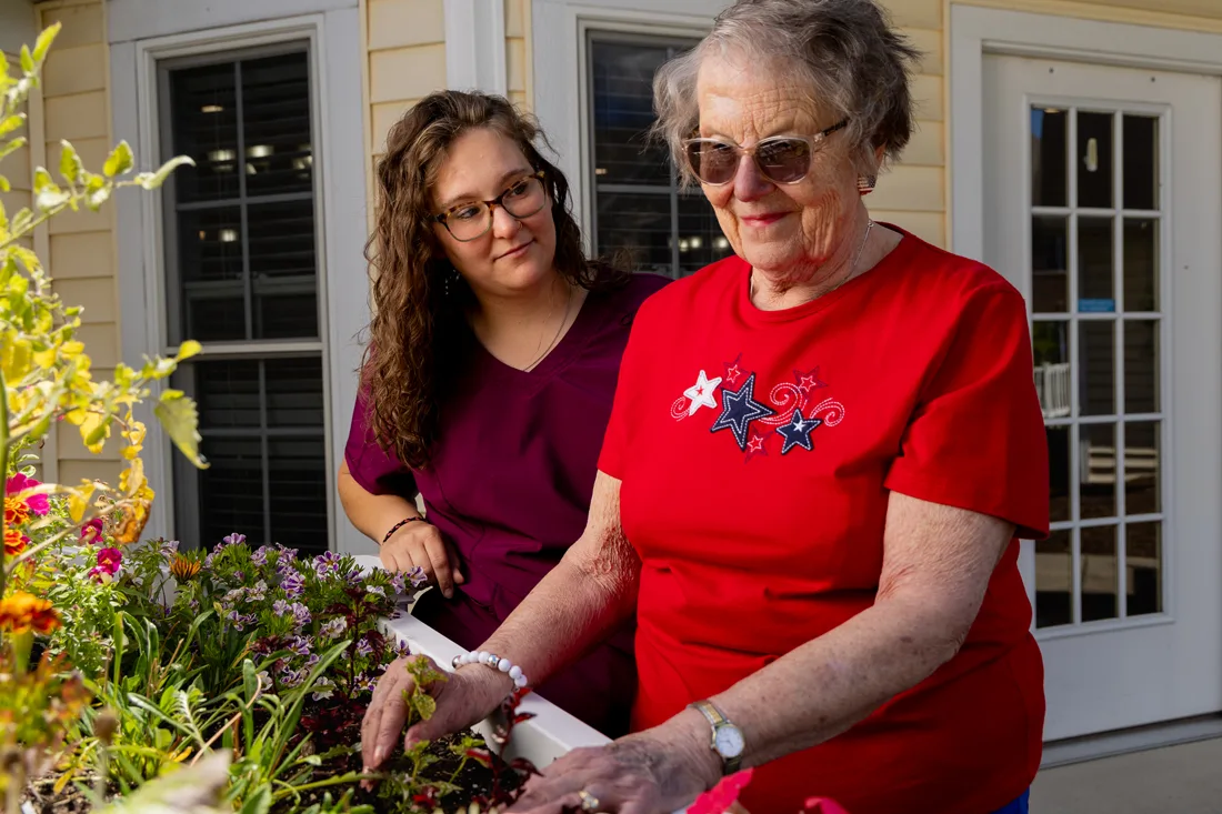 Caregiver standing with a smiling resident at a raised garden bed