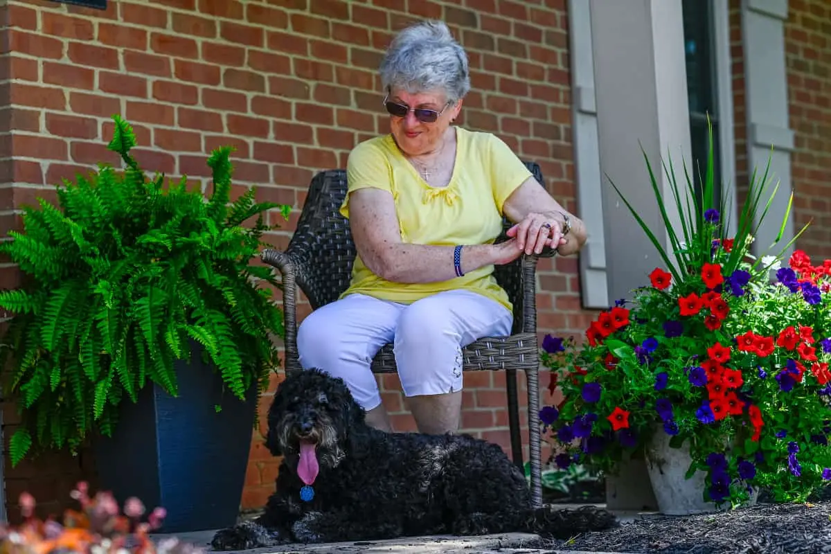 Independent living resident sitting outside with a black dog at her feet
